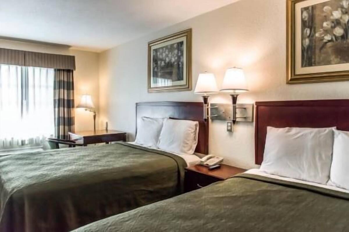 A hotel room with two beds, a nightstand with a lamp, a telephone, and framed artwork on the walls.