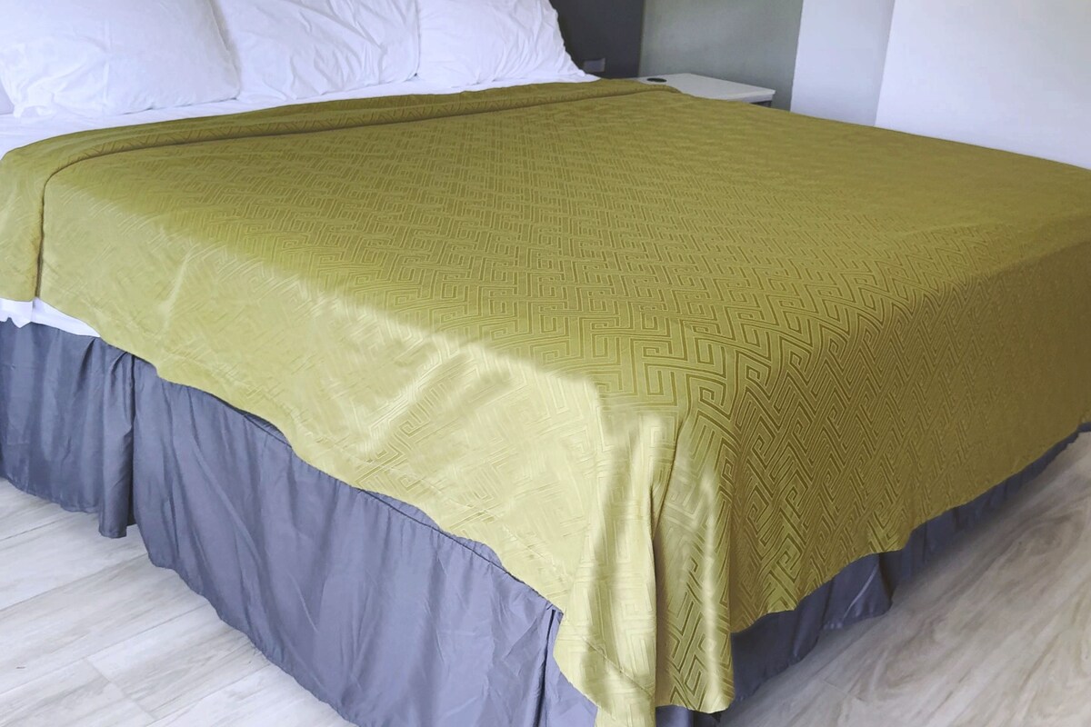 Una cama con colcha estampada, almohadas y una base con falda gris.