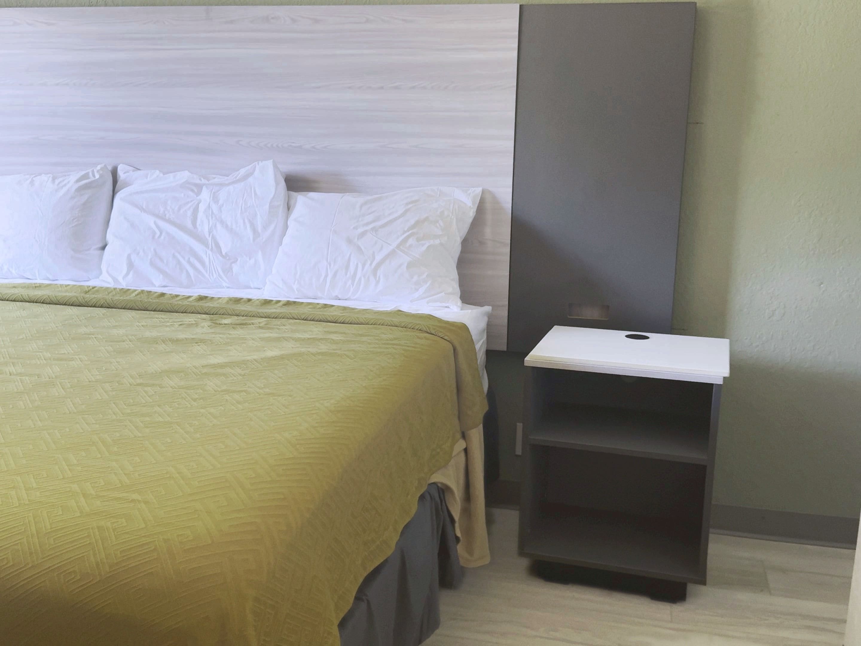 A hotel room with a bed, a nightstand, and a wall unit.