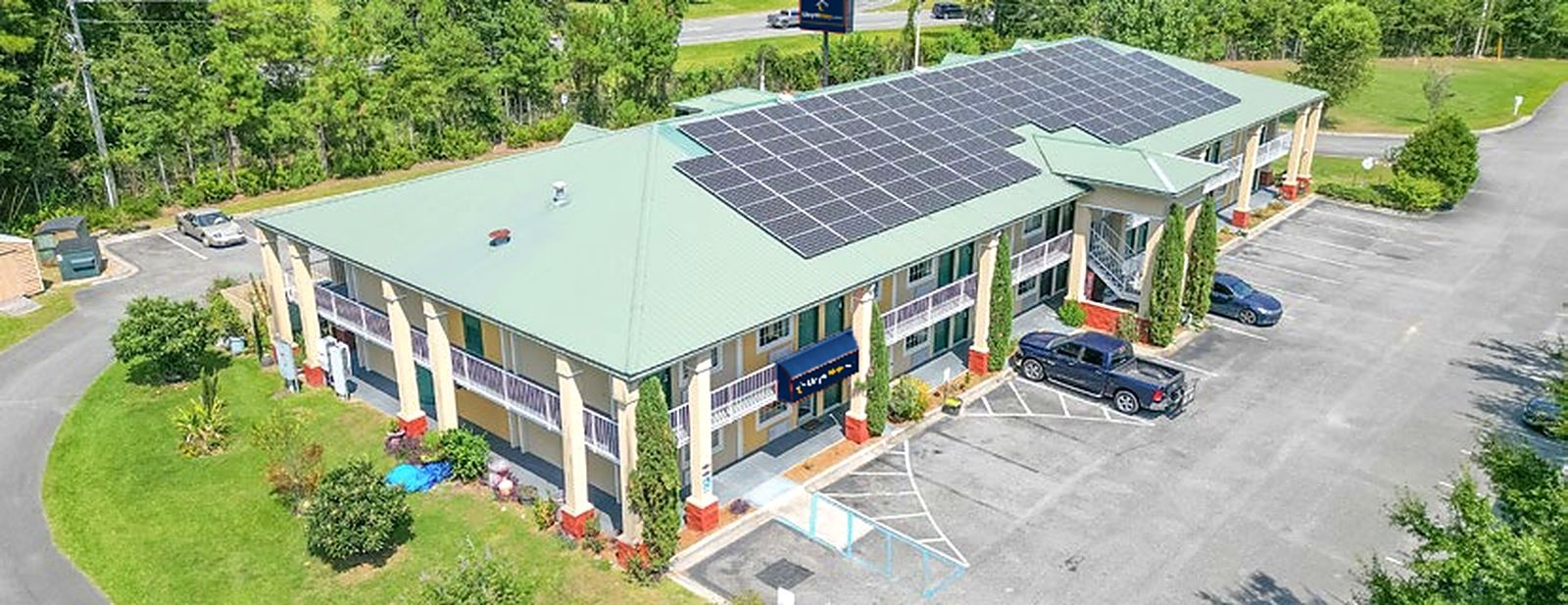 A building with a green roof, solar panels, a parking lot, and a small garden area.