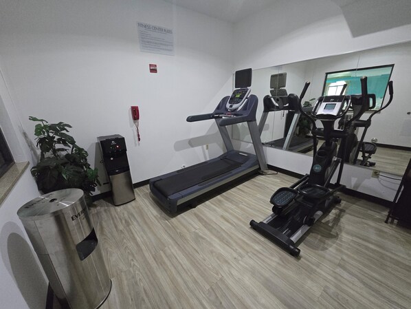 Un gimnasio con cinta de correr, elíptica y dispensador de agua.