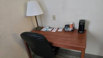 A wooden desk with a black office chair, a lamp, a coffee maker, and some papers.