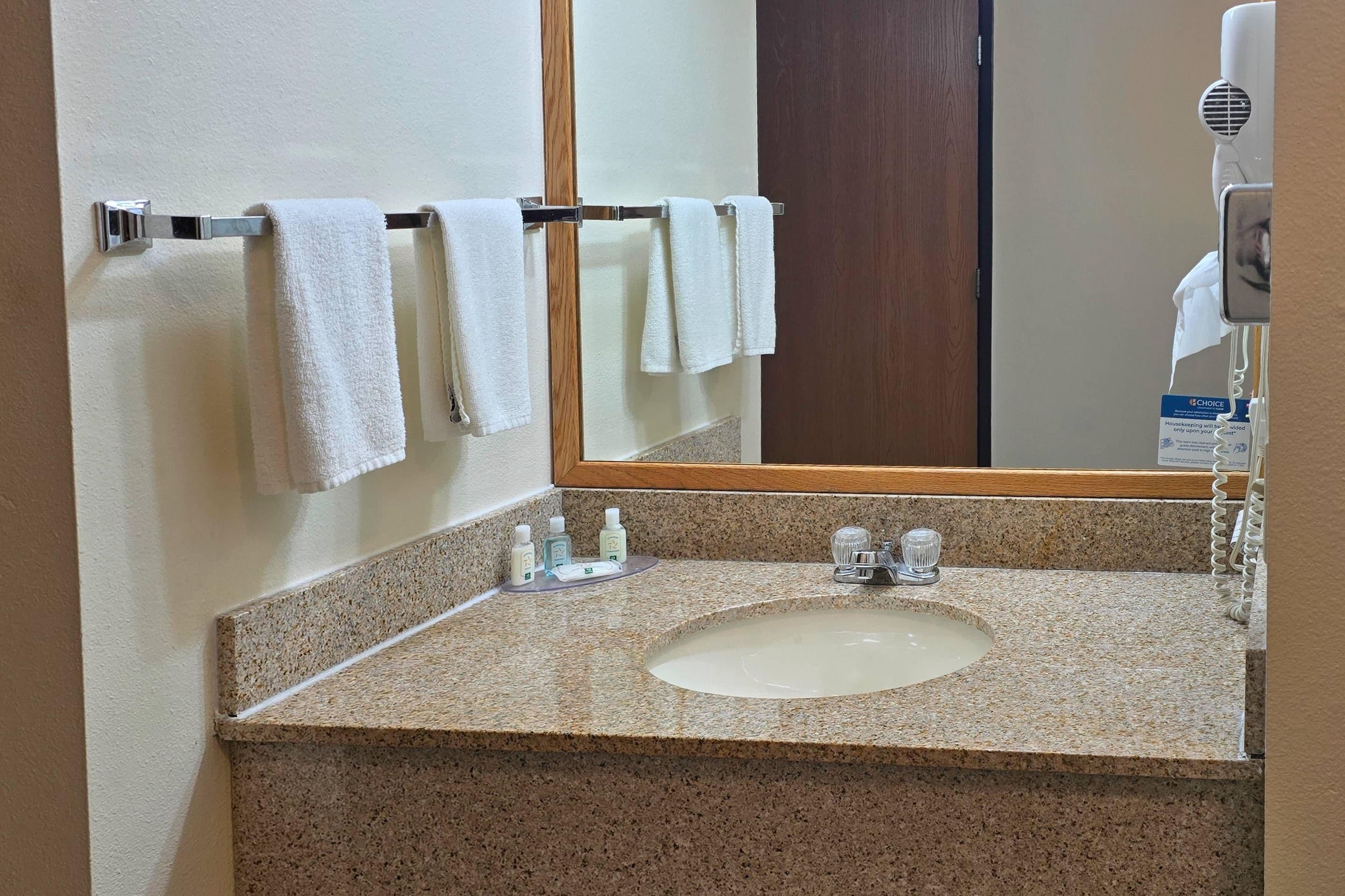 Baño con lavamanos de granito, espejo y toallero con varias toallas blancas.