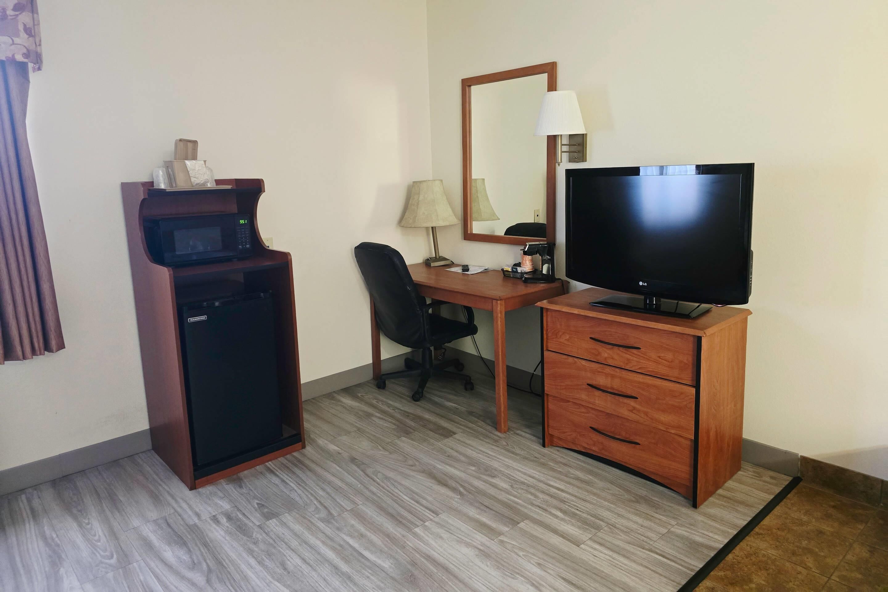 Une chambre d’hôtel équipée d’un bureau, d’une télévision, d’un four à micro-ondes, d’une chaise et d’un petit meuble de rangement.