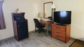 Une chambre d’hôtel équipée d’un bureau, d’une télévision, d’un four à micro-ondes, d’une chaise et d’un petit meuble de rangement.