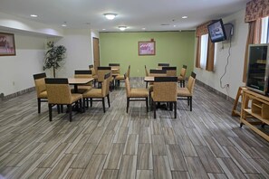 A dining area with multiple tables and chairs, a television mounted on the wall, and a plant in the corner.