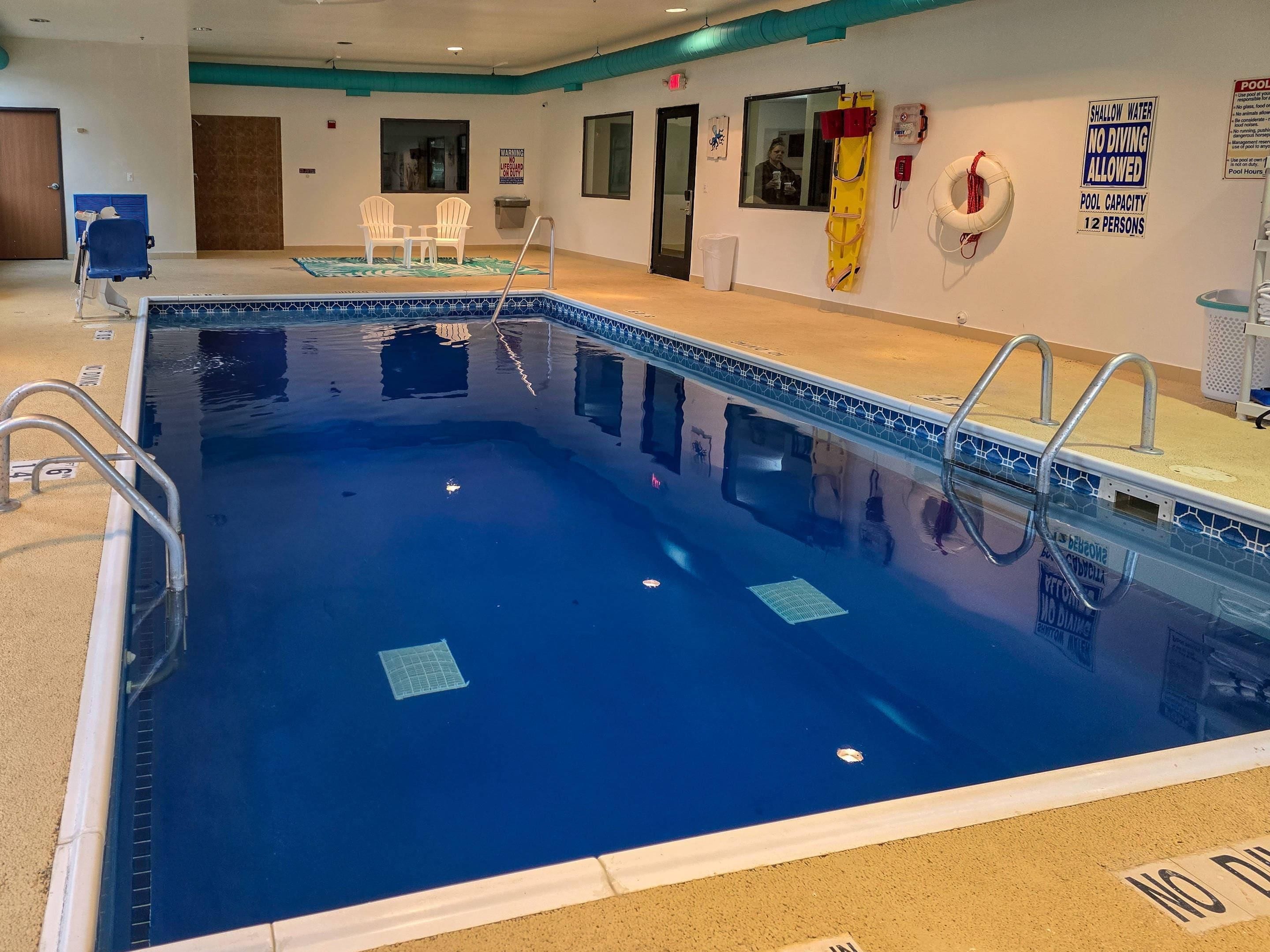 An indoor swimming pool with a lifeguard chair, a shallow water sign, and a capacity sign.