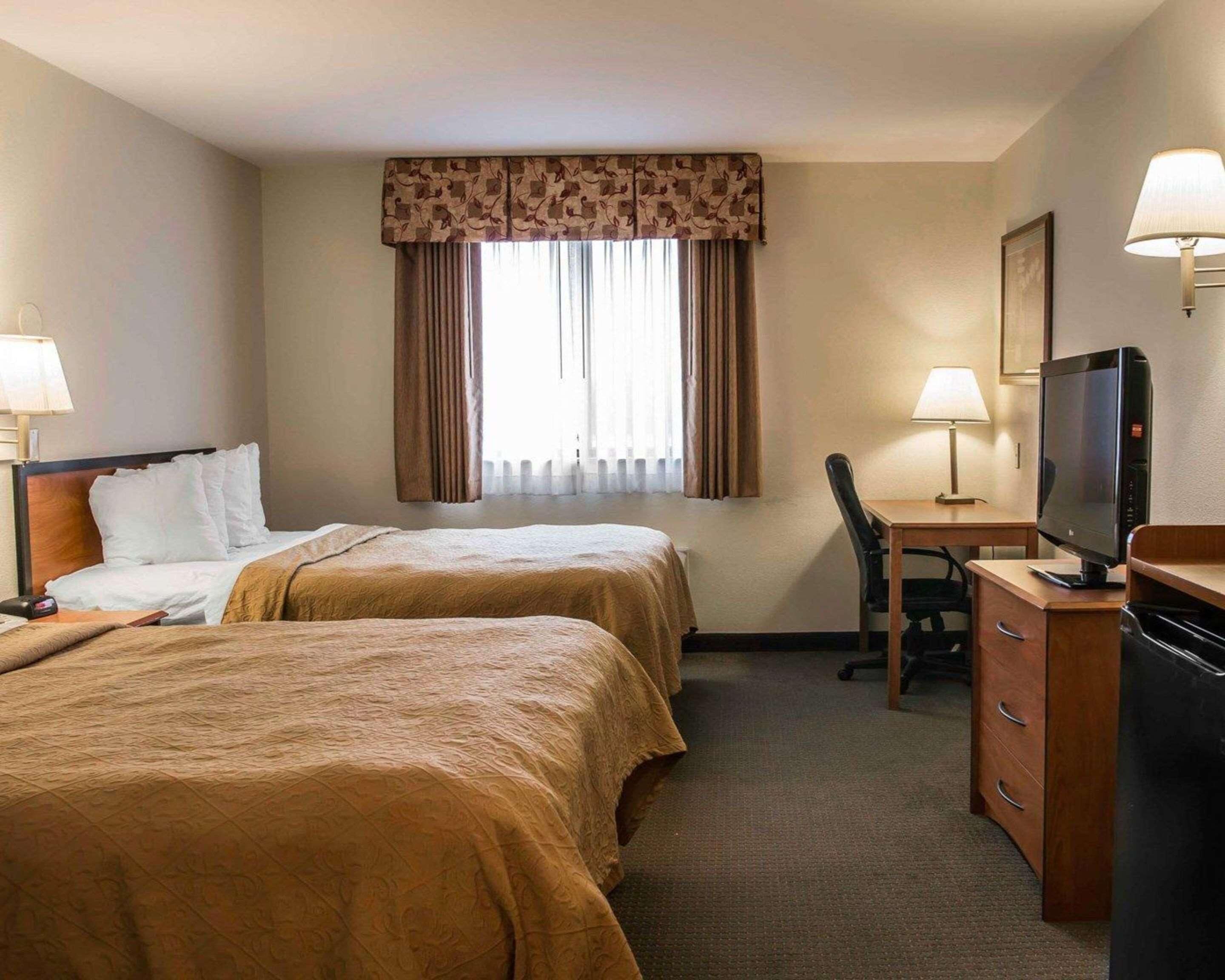A hotel room with two beds, a desk, a chair, a television, and a window with curtains.