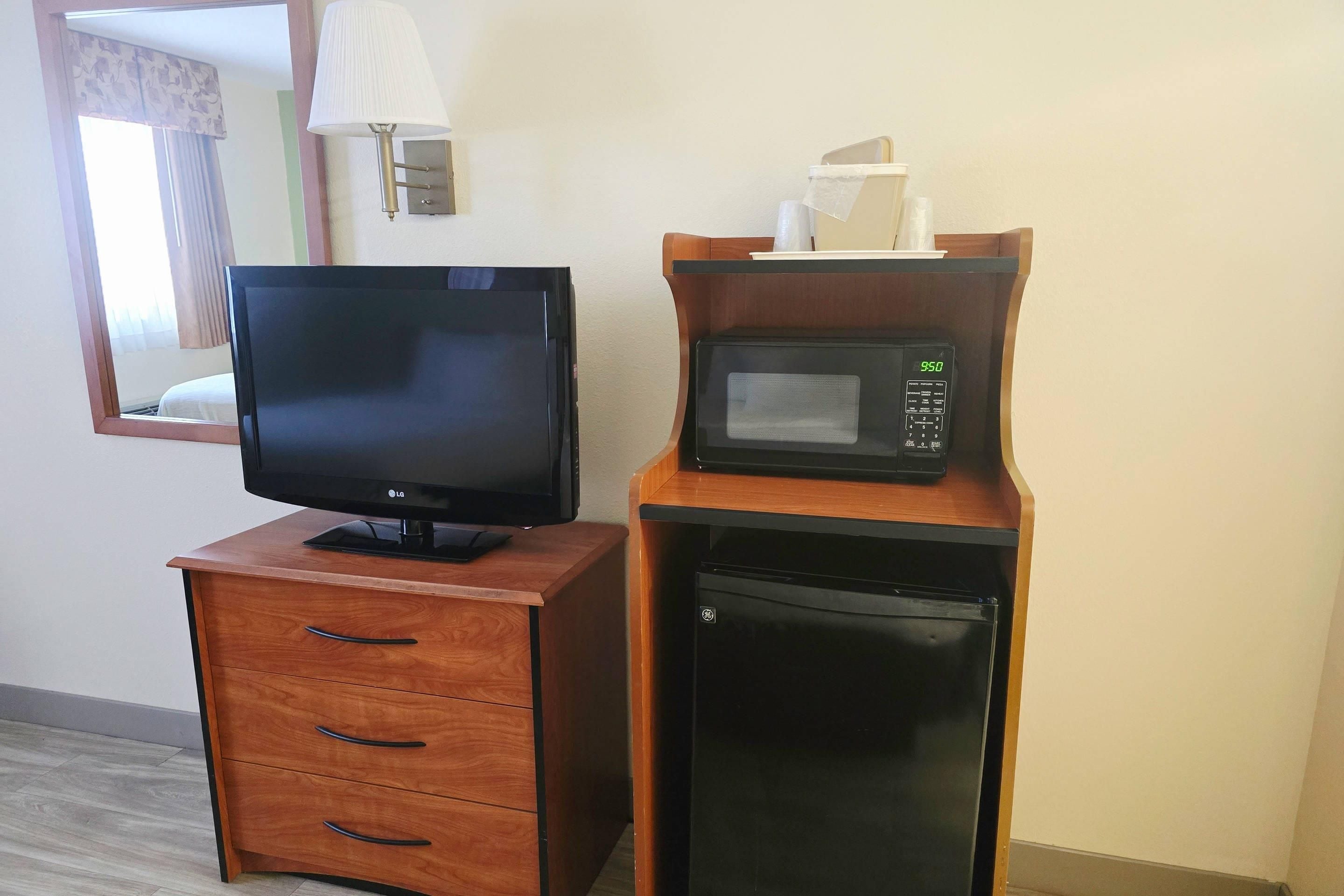 A wooden TV stand with a flat-screen TV, a microwave, and a small refrigerator in a hotel room.