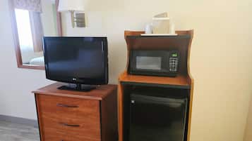A wooden TV stand with a flat-screen TV, a microwave, and a small refrigerator in a hotel room.