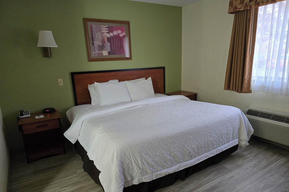 Una cama bien hecha en una habitación de hotel, con cabecera de madera, una mesita de noche con lámpara y un cuadro en la pared.