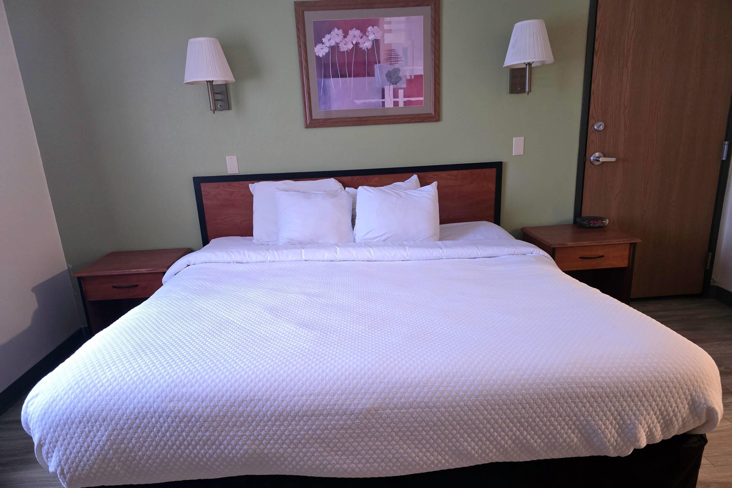 A neatly made bed with white bedding, two bedside tables with lamps, and a framed artwork on the wall.