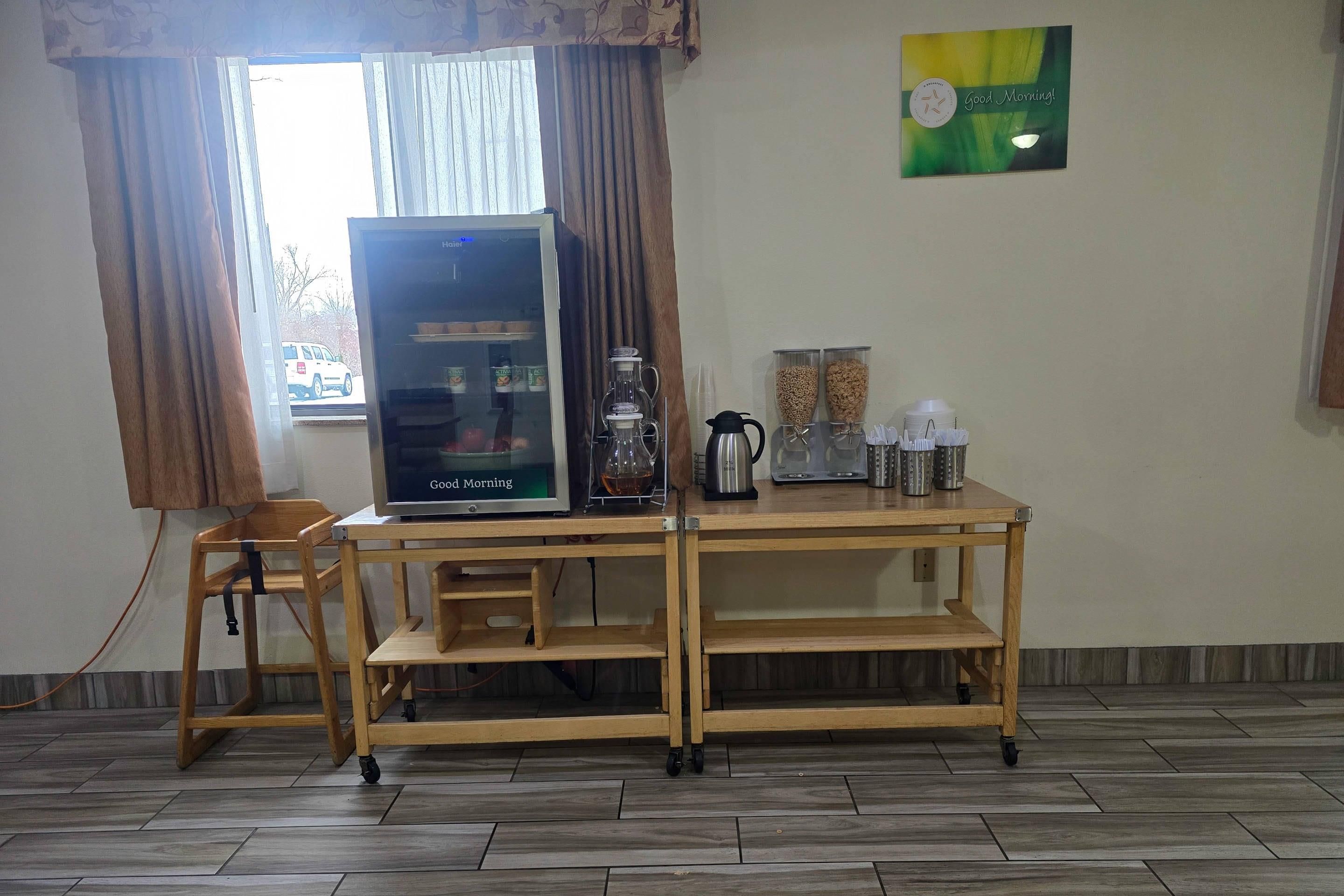 A room with a wooden table, a refrigerator, a coffee maker, and a window with curtains.