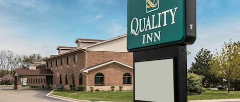 Un letrero de Quality Inn con un edificio de ladrillo al fondo.