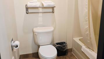 Un baño con inodoro, repisas con toallas, un bote de basura y una bañera.