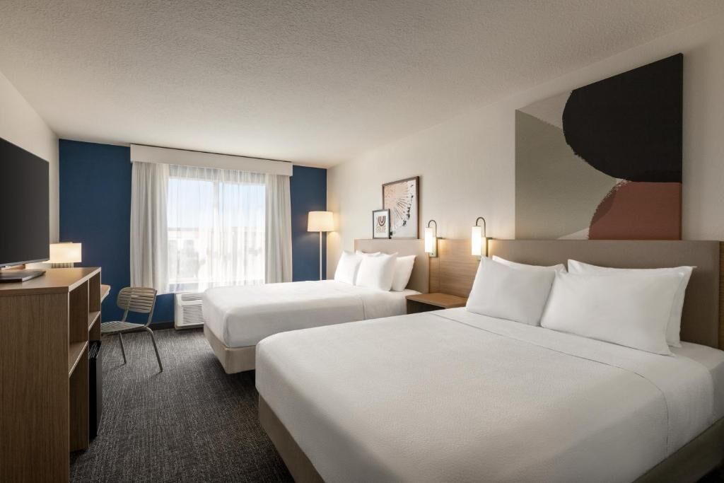 A hotel room with two beds, a desk, a chair, and a large abstract painting on the wall.