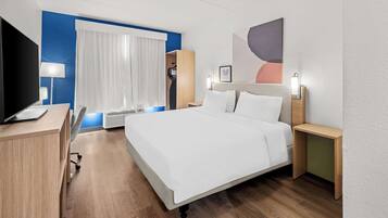 A hotel room with a bed, a desk, a TV, a window with curtains, and a wall with a picture.
