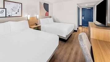 A hotel room with two beds, a desk, a chair, a TV, and artwork on the walls.