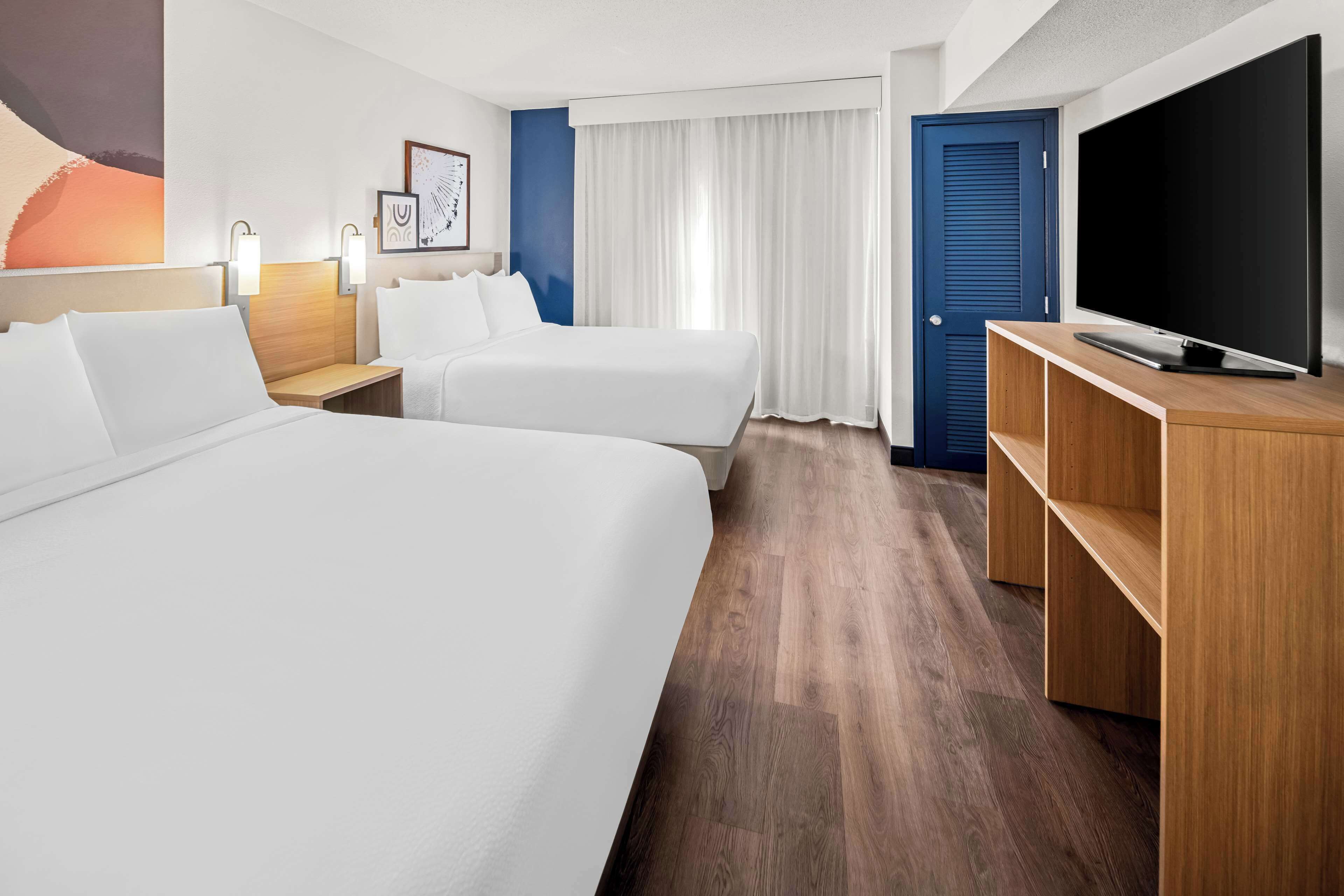 Una habitación de hotel con dos camas, televisión, escritorio y un amplio ventanal con cortinas.