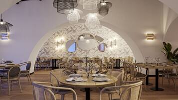 Restaurante com mesas redondas, cadeiras de vime e luminárias pendentes.