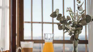 Un desayuno con una taza de café, un vaso de jugo de naranja, huevos revueltos y un florero con flores sobre una mesa.