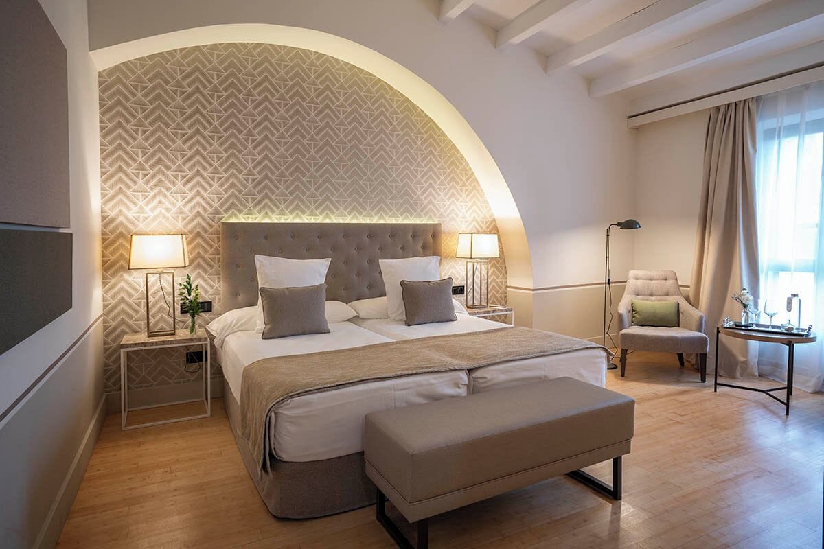 Een moderne hotelkamer met een groot bed, een bankje, een stoel en een bureau met een lamp.