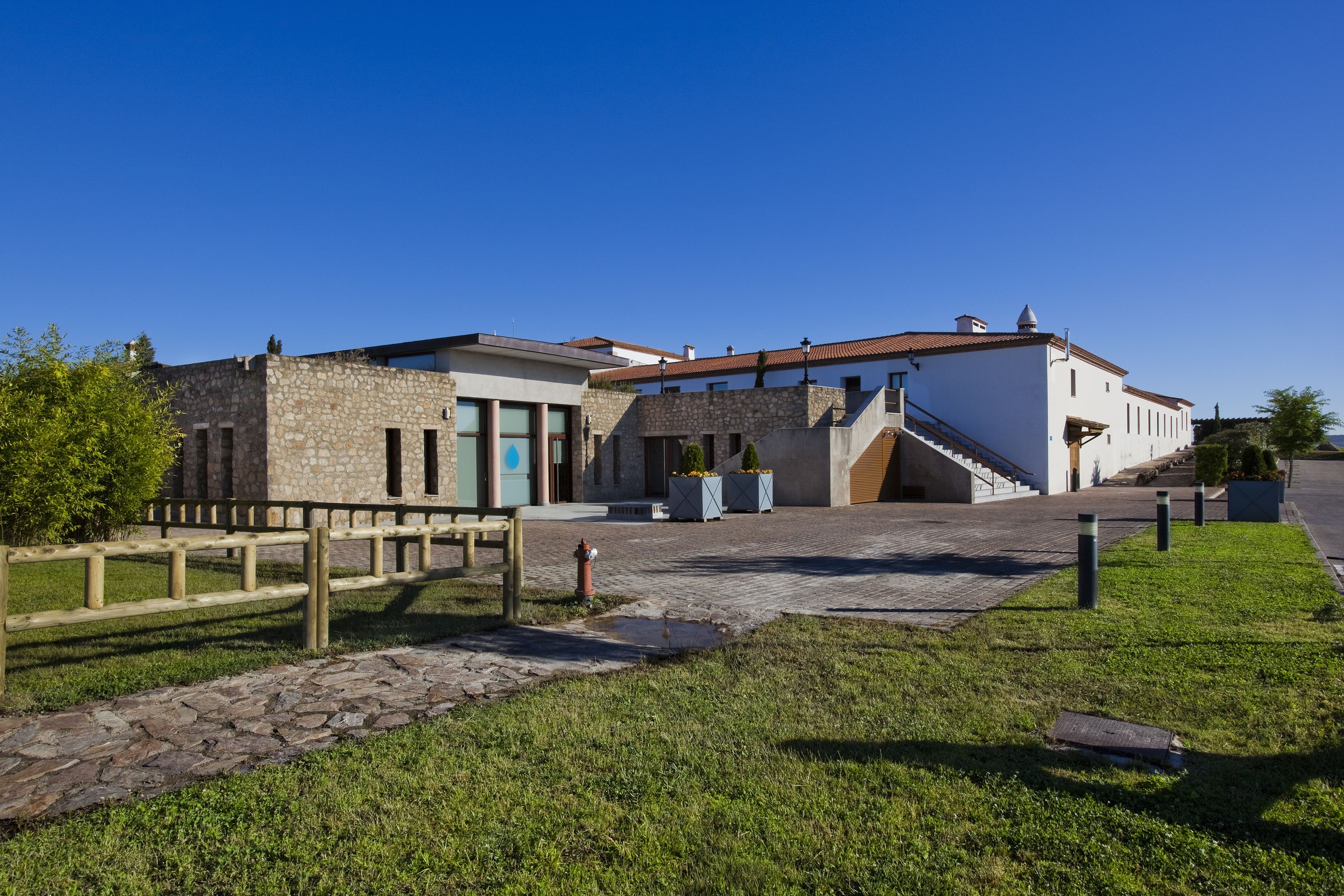 Un edificio de fachada de piedra, cerca de madera y zona de entrada pavimentada.
