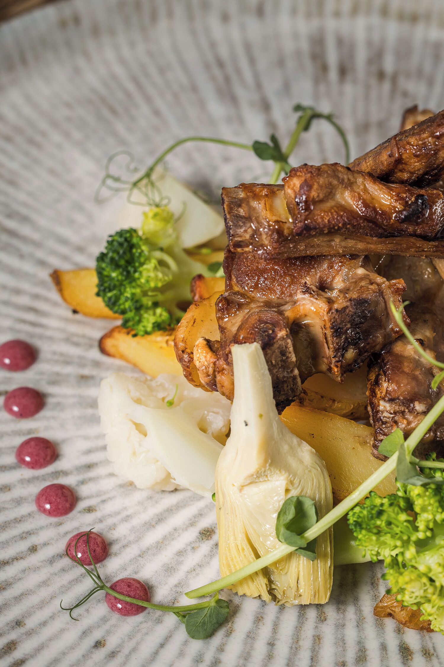 A plate of food with roasted meat, potatoes, broccoli, and artichokes.