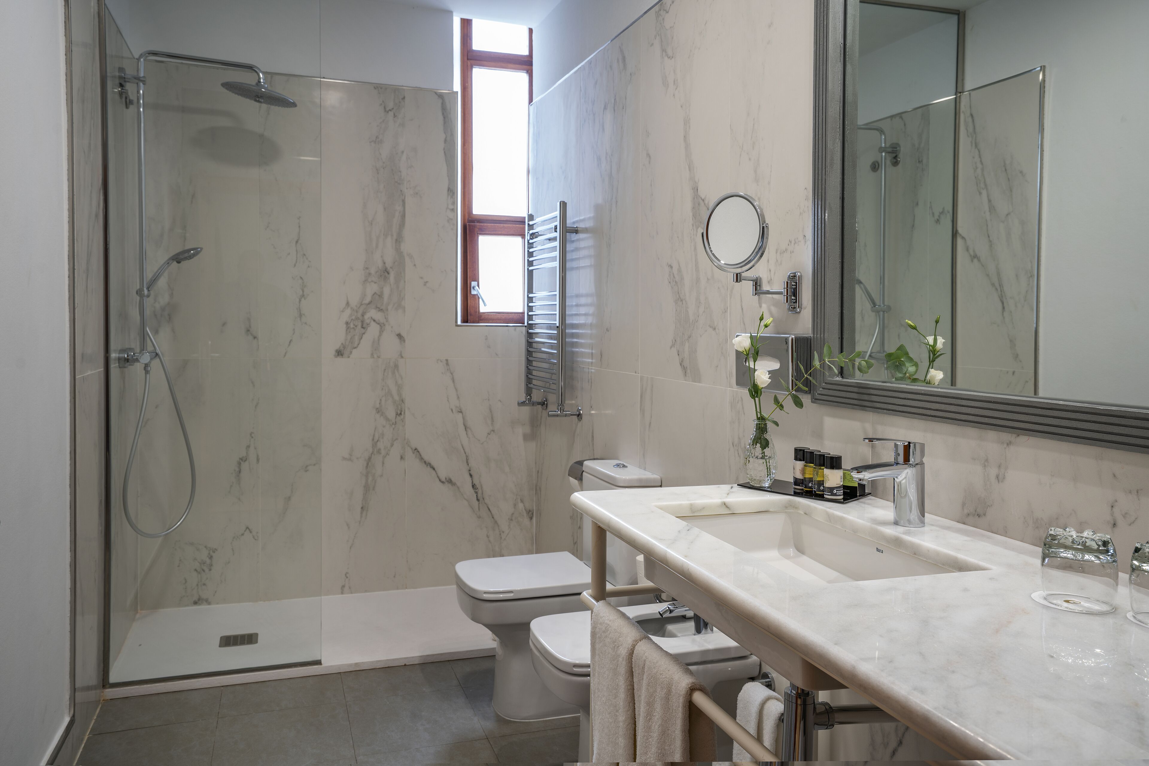 A modern bathroom with a glass-enclosed shower, a toilet, and a vanity with a large mirror.