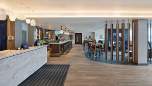 A modern hotel lobby with a reception desk, bar area, and seating for guests.