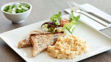 Un piatto con uova strapazzate, pane tostato e un'insalata.