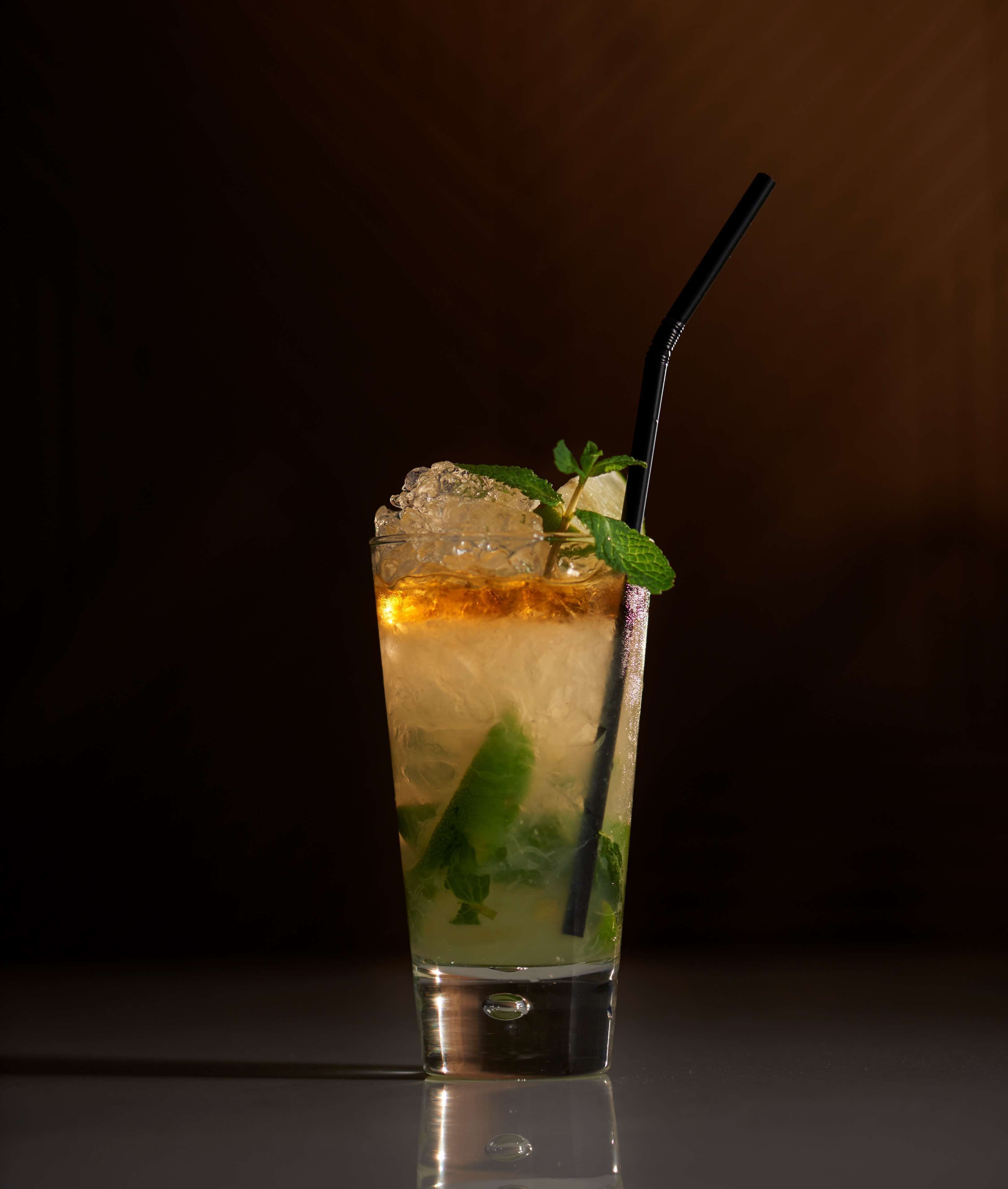 A tall glass with a clear liquid, ice cubes, and mint leaves, with a black straw.
