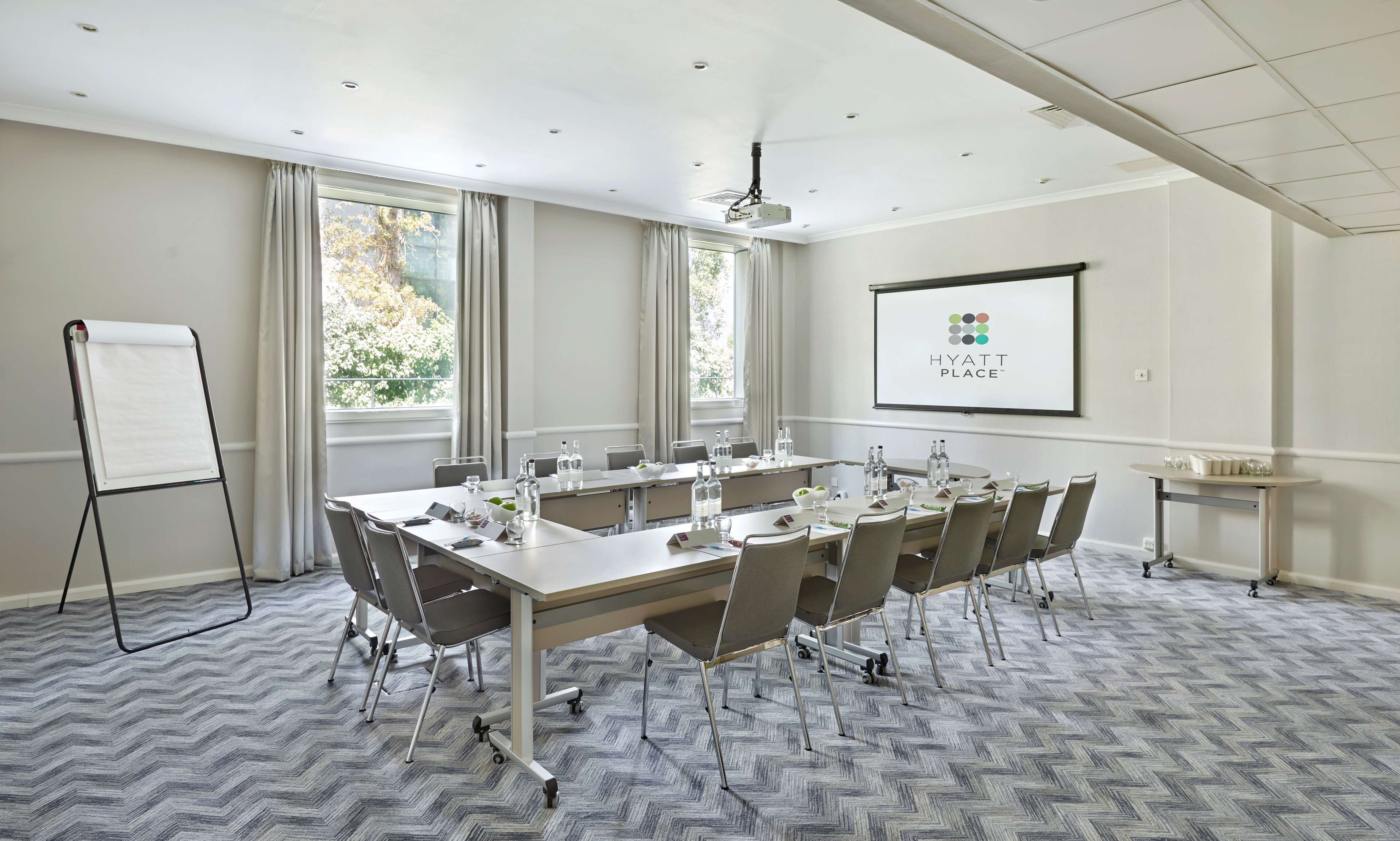 A conference room with a large table, chairs, a whiteboard, and a projector screen displaying the Hyatt Place logo.