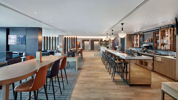 A modern hotel lobby with a long reception desk, bar area, and seating for guests.