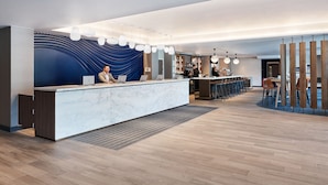 A modern hotel lobby with a marble reception desk, bar area, and wooden flooring.