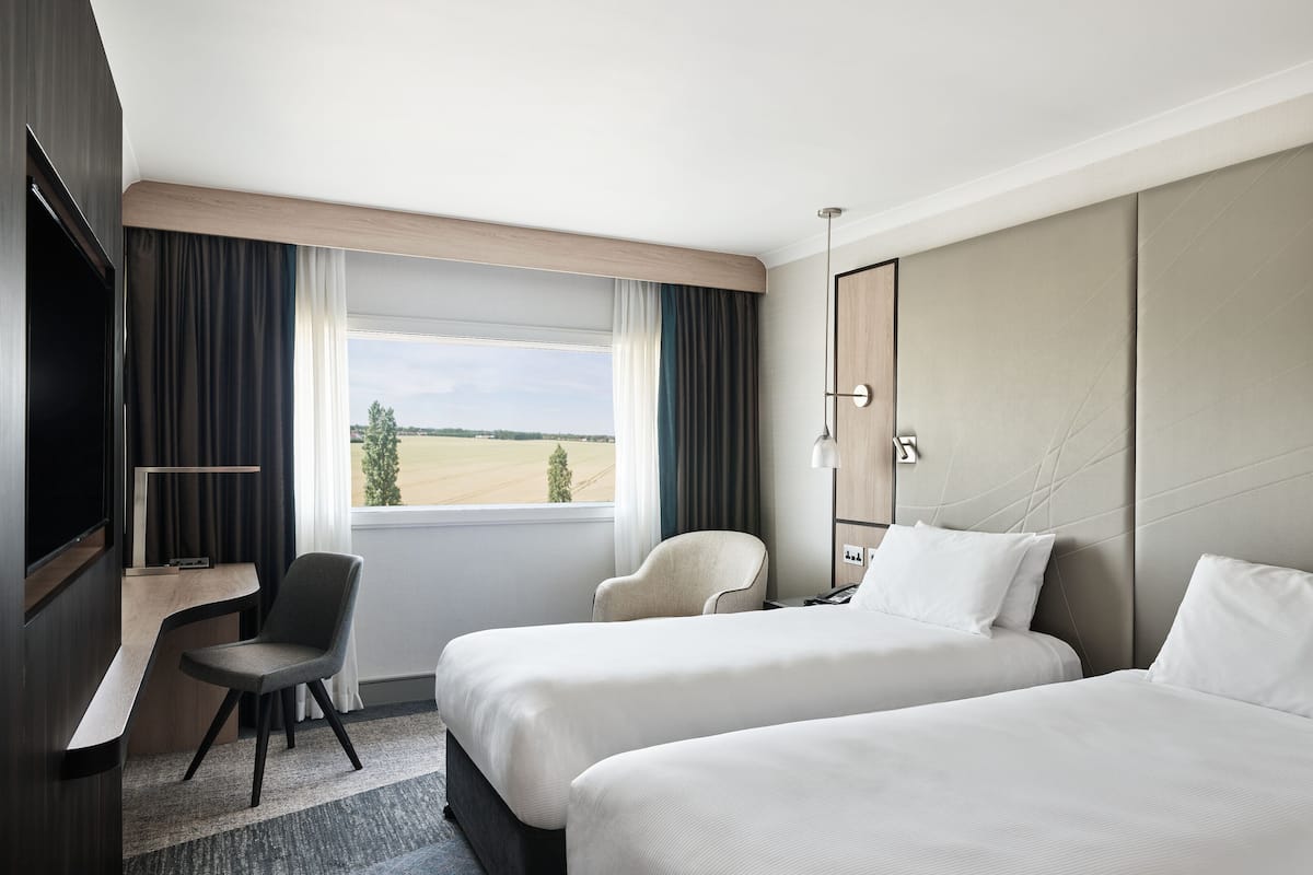 Une chambre d’hôtel avec deux lits, un bureau, une chaise, une télévision et une fenêtre donnant sur la campagne.