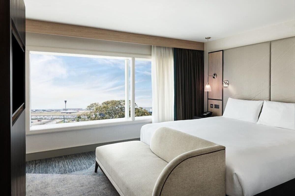 Une chambre d’hôtel avec un grand lit, un coin salon, une fenêtre donnant sur un aéroport et un téléphone fixé au mur.
