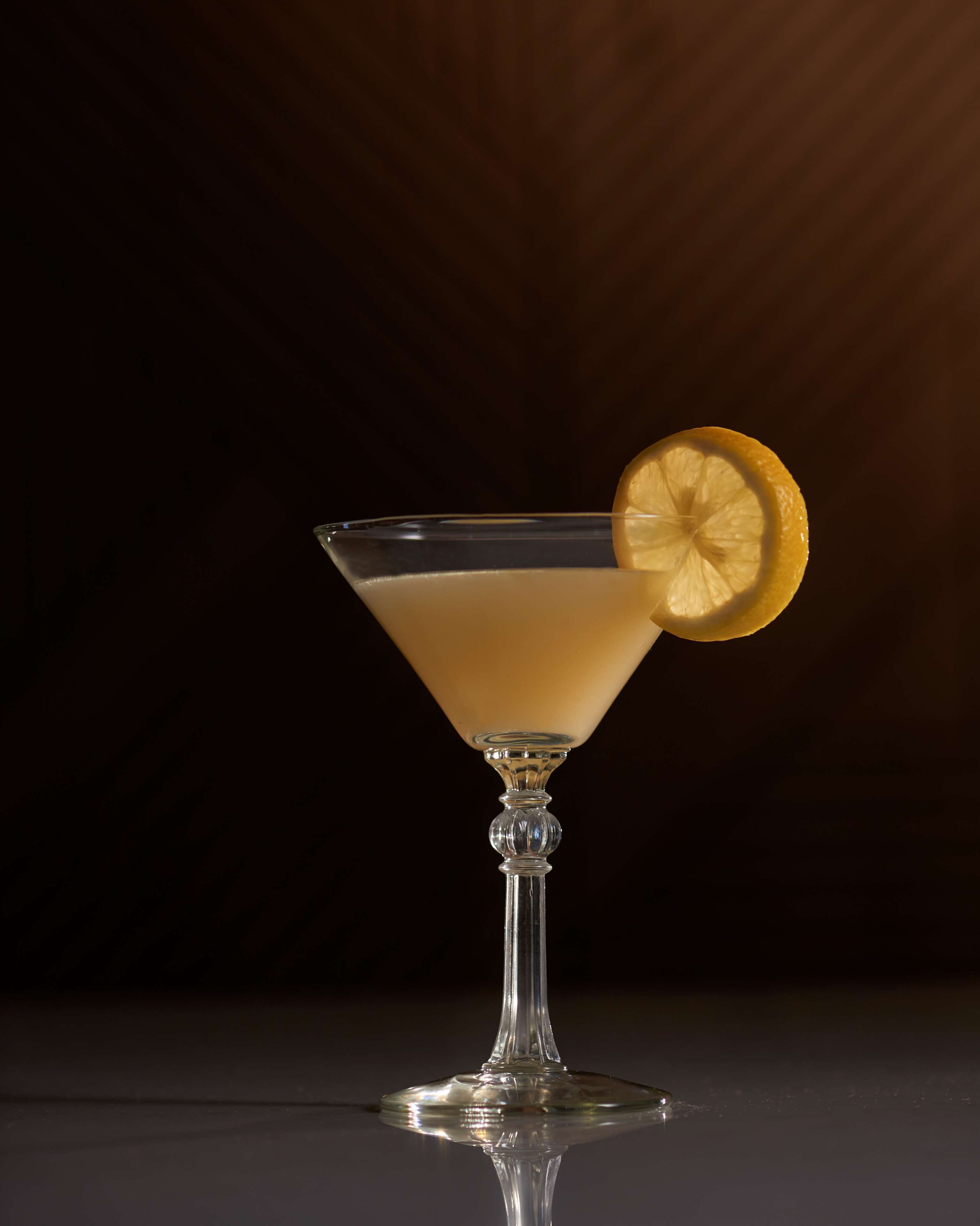 Un verre à martini, orné d’une tranche de citron, posé sur une surface réfléchissante.