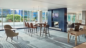 A modern office space with a large meeting table, comfortable seating, a television screen, and a view of the outdoors.
