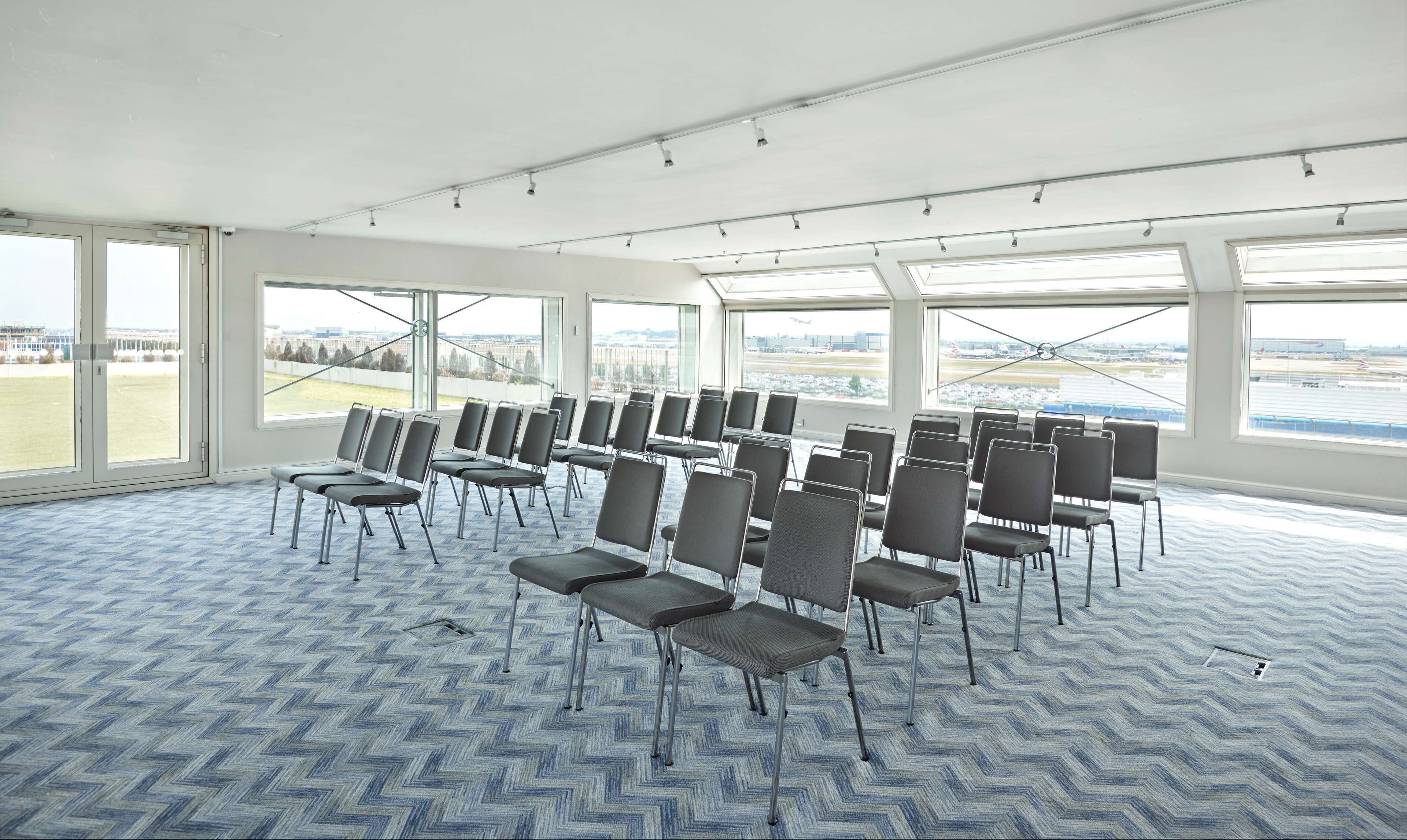 A conference room with rows of chairs, large windows, and a view of an airport.