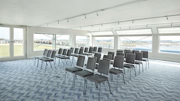 A conference room with rows of chairs, large windows, and a view of an airport.