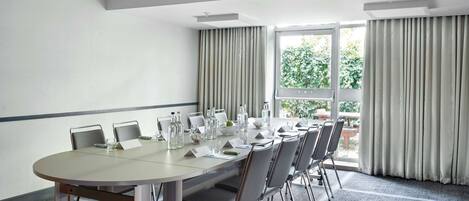 A conference room with a round table, chairs, and a projector screen.