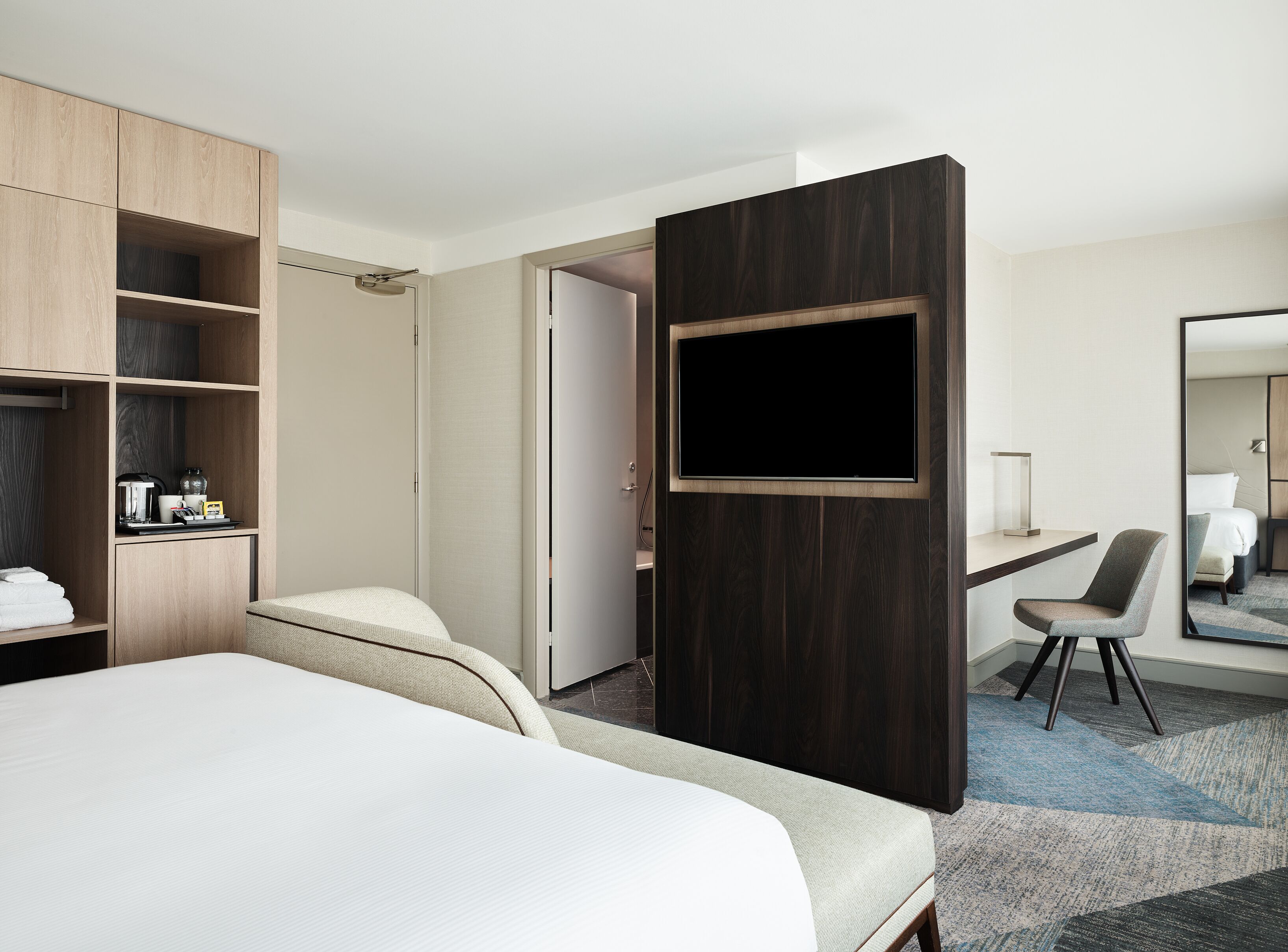 A hotel room with a bed, a desk, a chair, a TV, and a wardrobe.