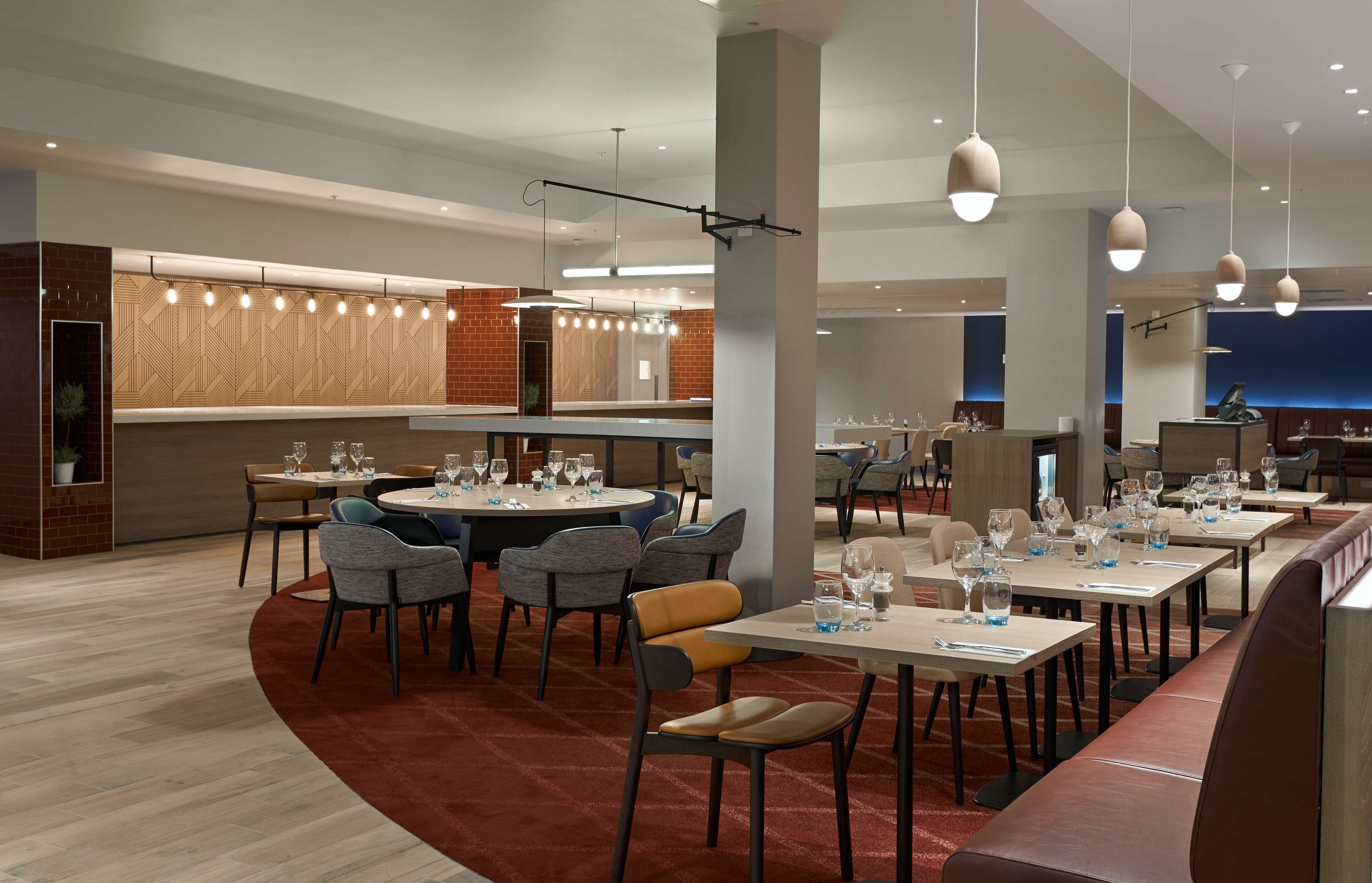 A modern restaurant with round tables, chairs, and hanging pendant lights.
