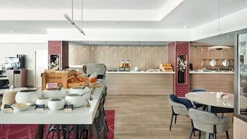 A modern dining area with a long table, chairs, and a counter with food and drink options.