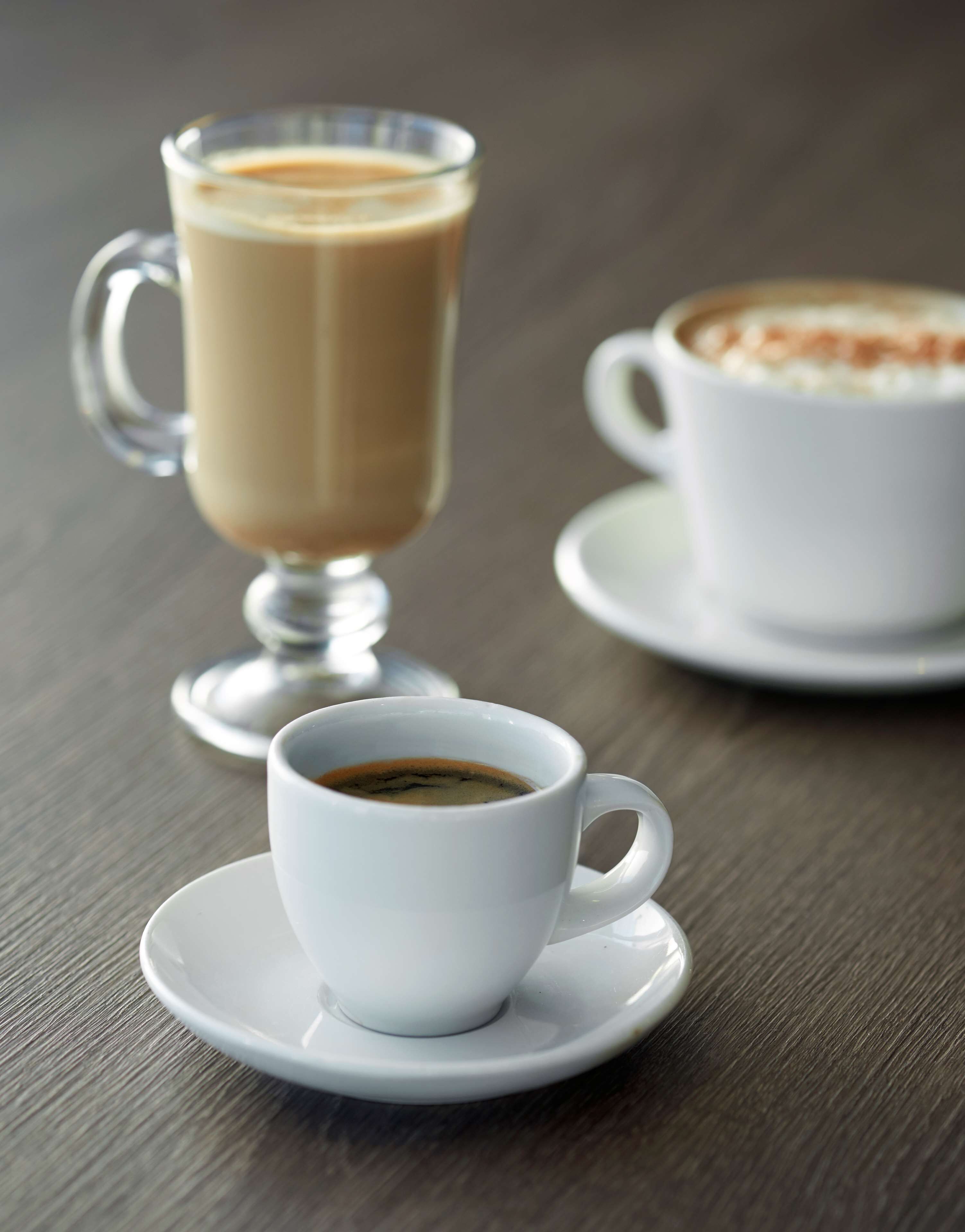 Un verre transparent contenant un expresso et une tasse blanche de café sur une table en bois.