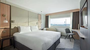Une chambre d’hôtel moderne avec un grand lit, un bureau et une vue sur un aéroport.