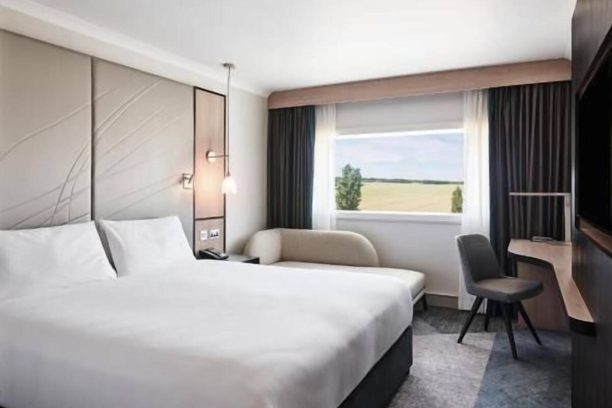 Une chambre d’hôtel avec un grand lit, un bureau, une chaise et une fenêtre donnant sur la campagne.