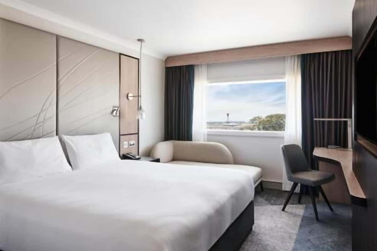 Une chambre d’hôtel avec un grand lit, un bureau, une chaise et une vue sur la ville.
