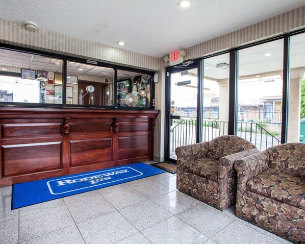 A reception area with a wooden desk, a blue mat with "RODEWAY INN" logo, and two floral-patterned sofas.